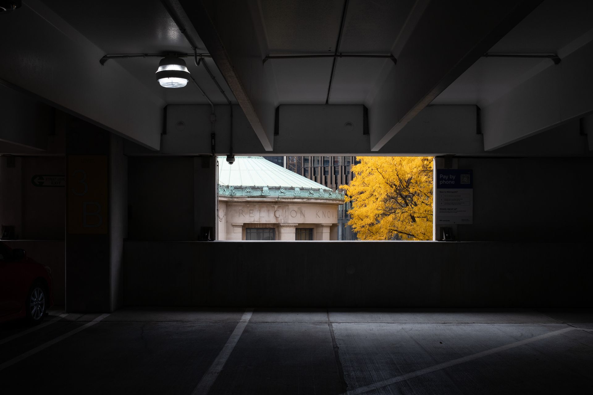 A parking garage with a window looking out to a building and a tree.