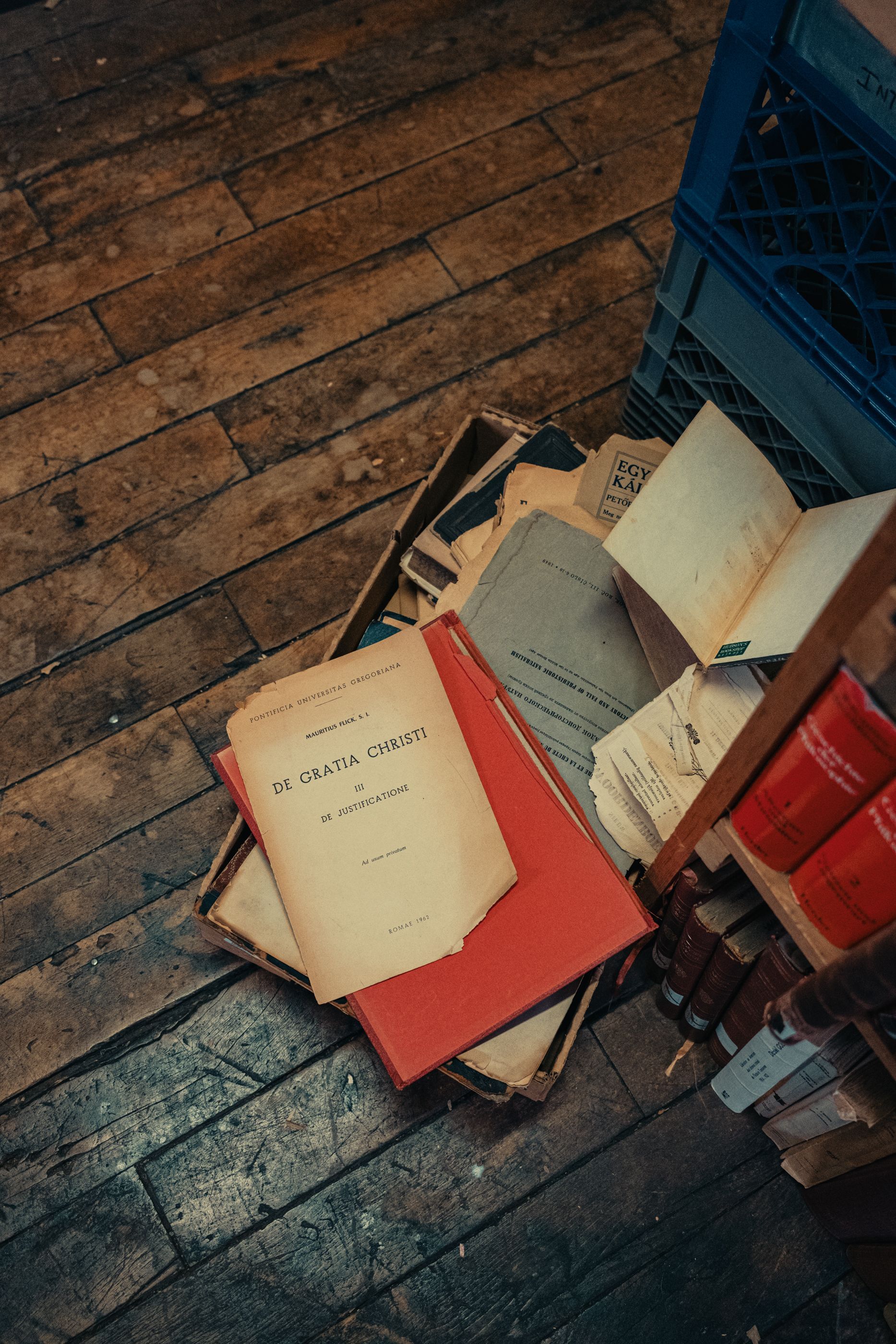 A stack of books on a wooden floor next to a shelf.