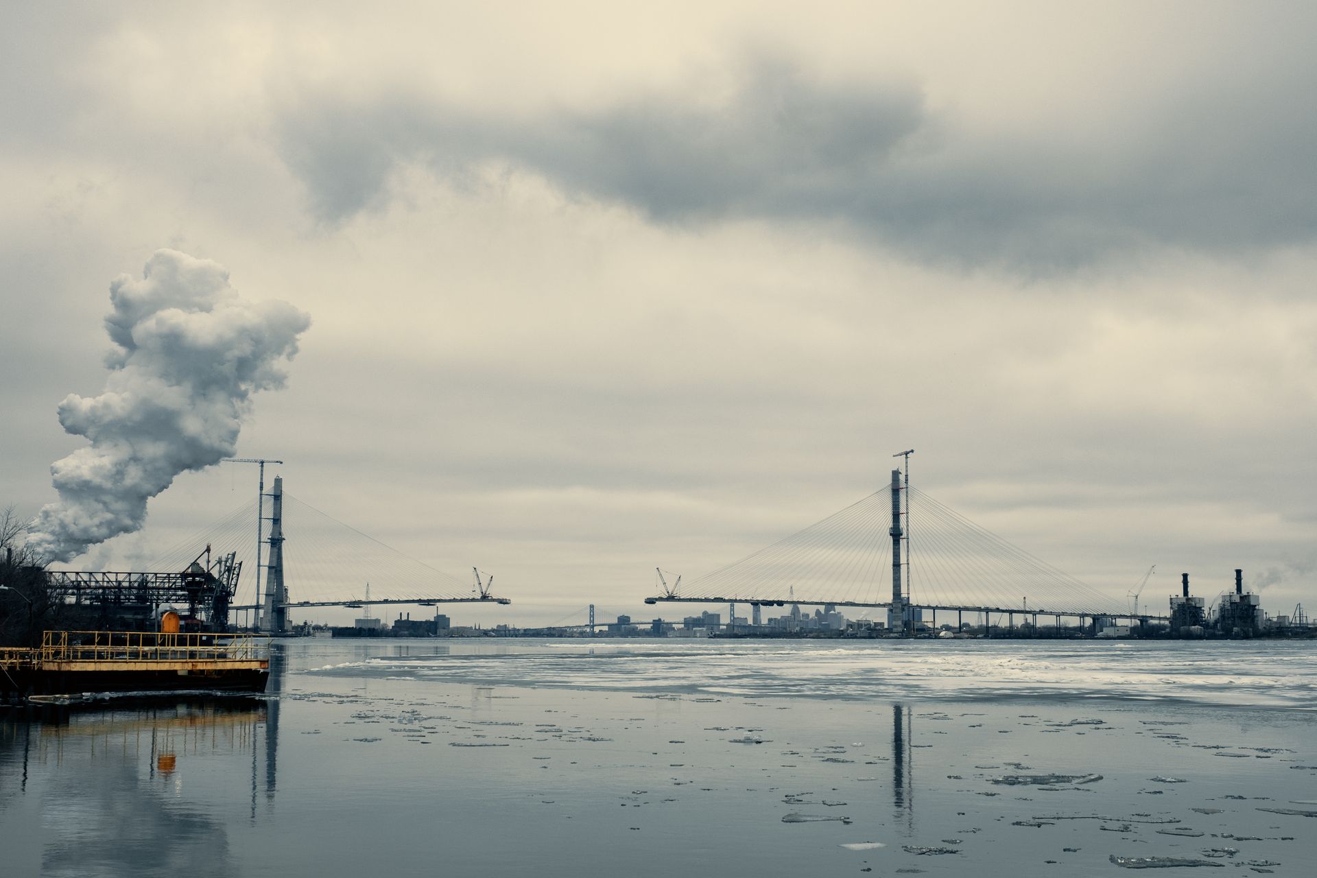 A bridge over a body of water with a factory in the background.