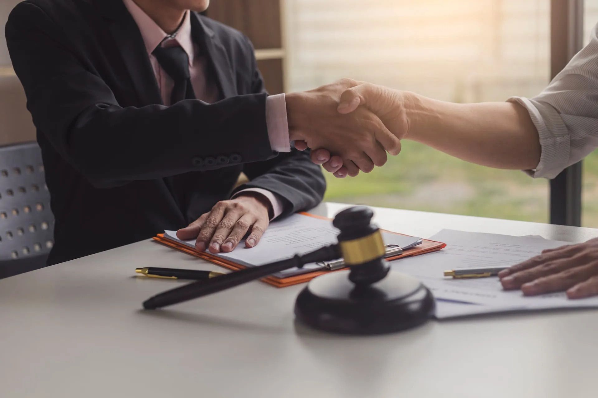 Deux personnes se serrent la main au-dessus d'une table où se trouvent des documents et un maillet, signifiant un accord.
