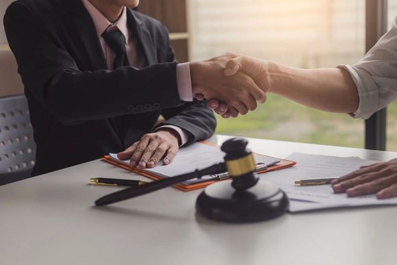 Deux personnes se serrent la main au-dessus d'une table où se trouvent des documents et un maillet, signifiant un accord.