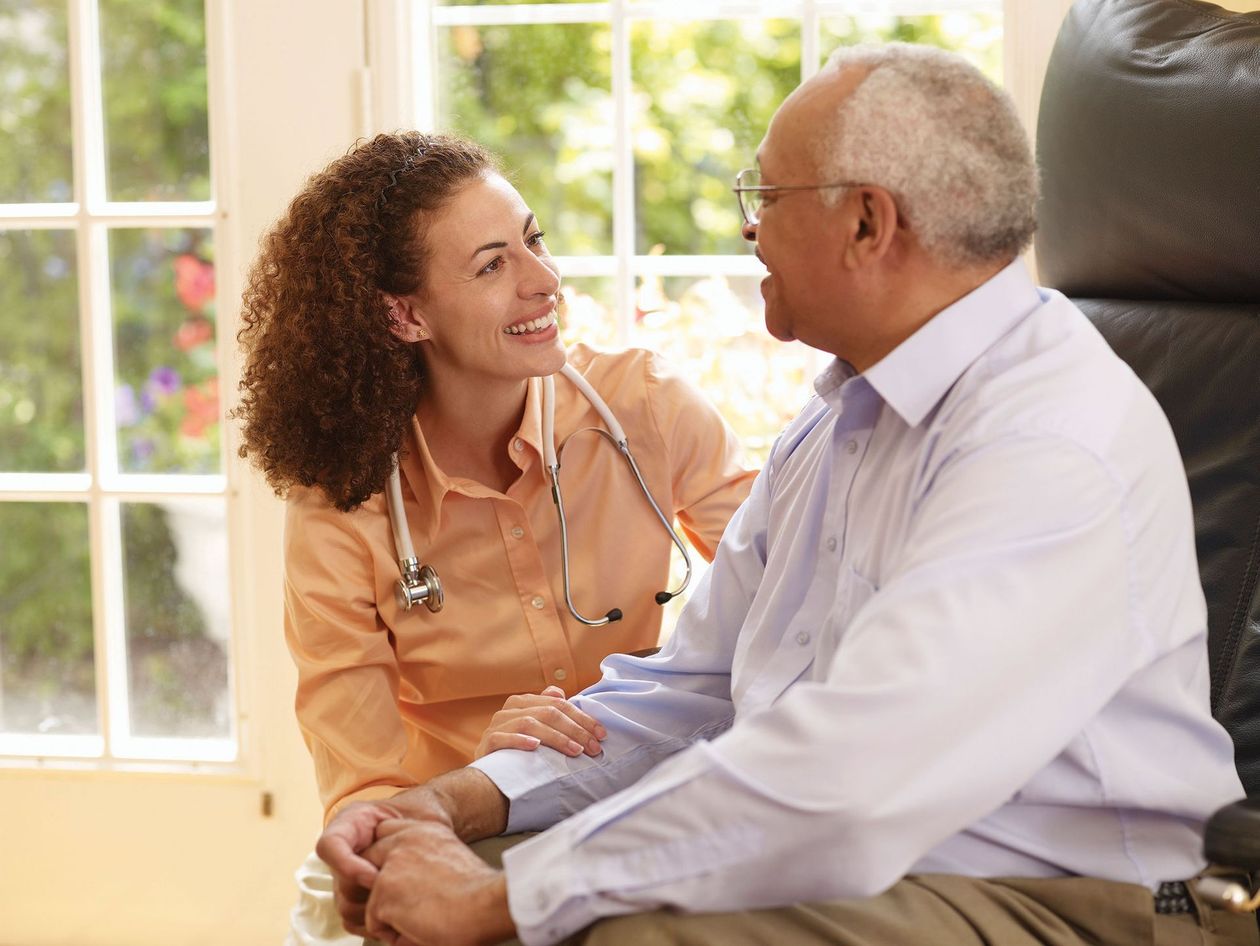 A nurse is talking to an elderly man in a chair.