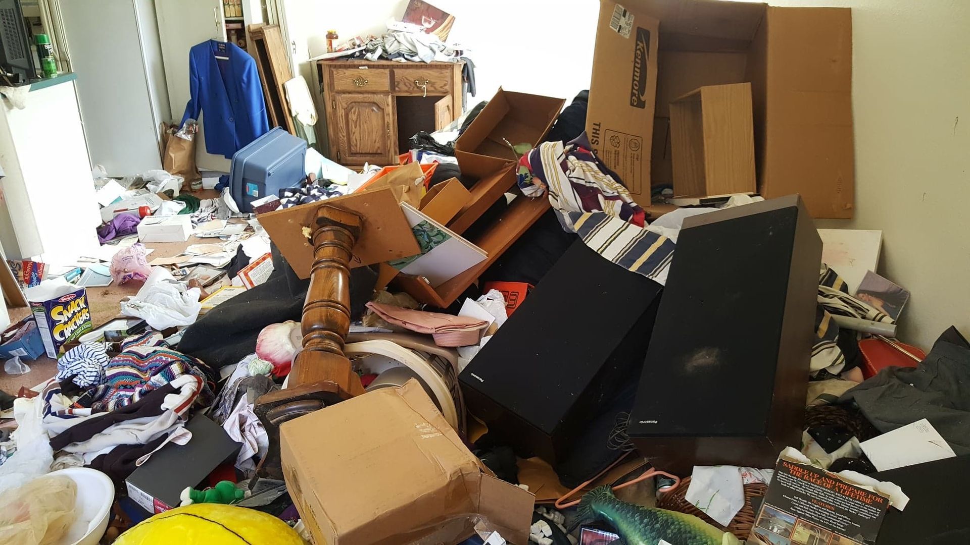 A cluttered room filled with piled boxes, clothes, and scattered debris.