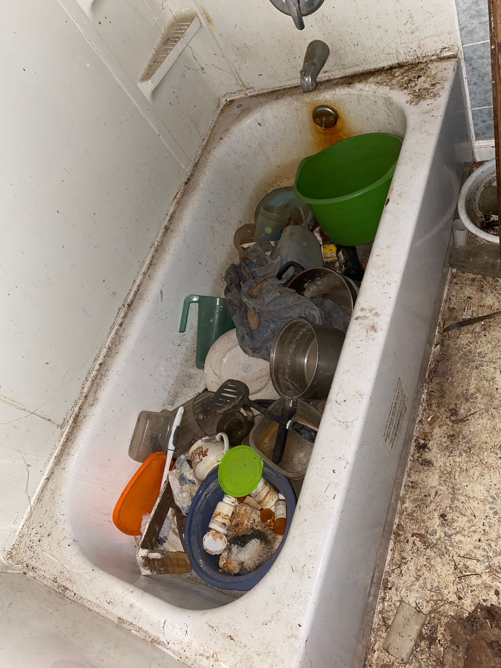 Dirty bathtub filled with scattered dishes, cups, and utensils