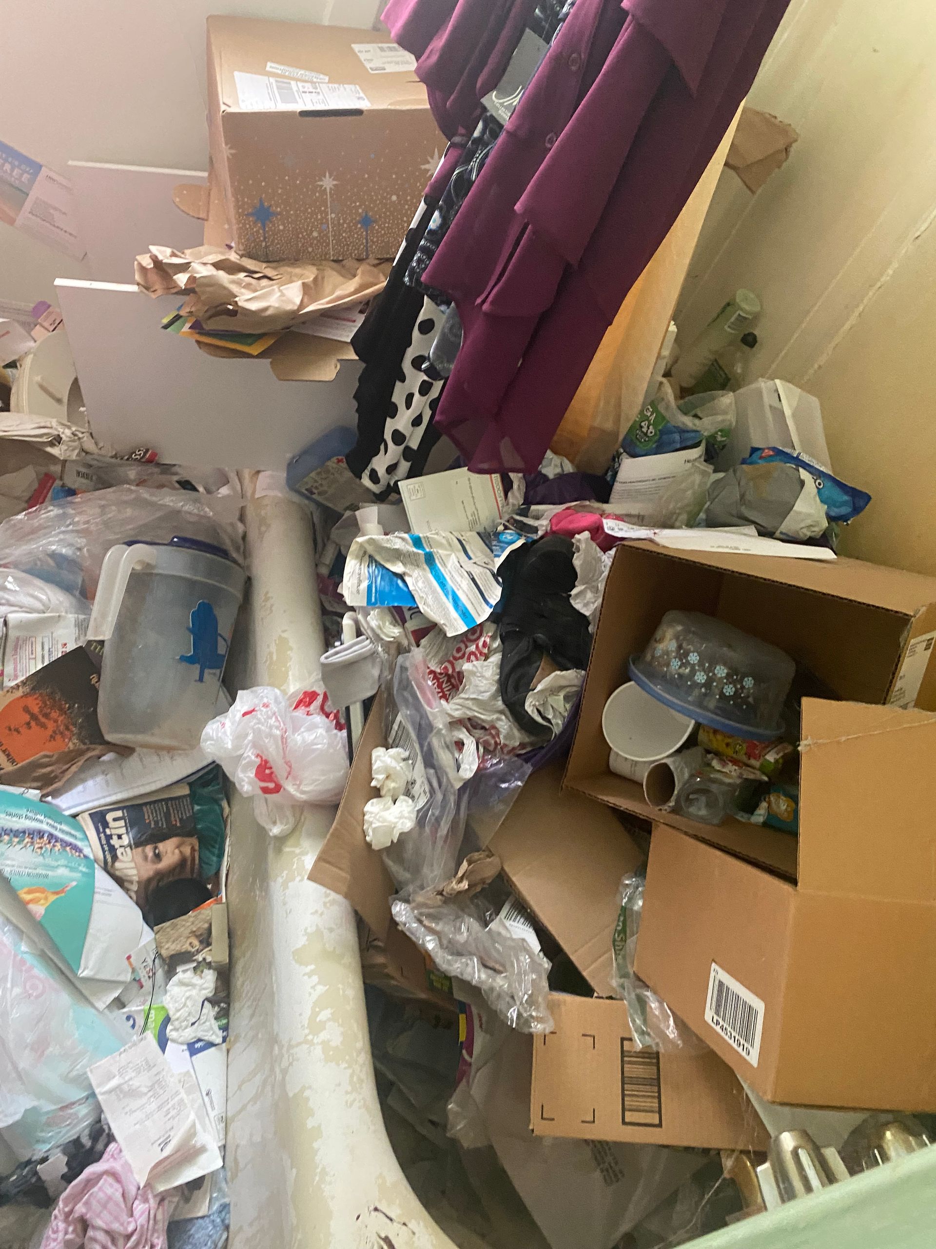 Cluttered room with overflowing trash bags, cardboard boxes, and scattered household debris.