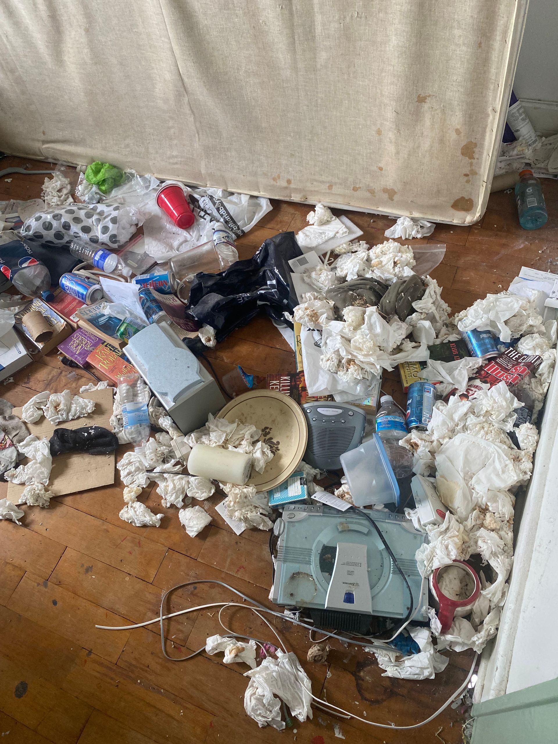 Cluttered floor with scattered trash, broken items, foam debris, and a tipped device beside a couch.
