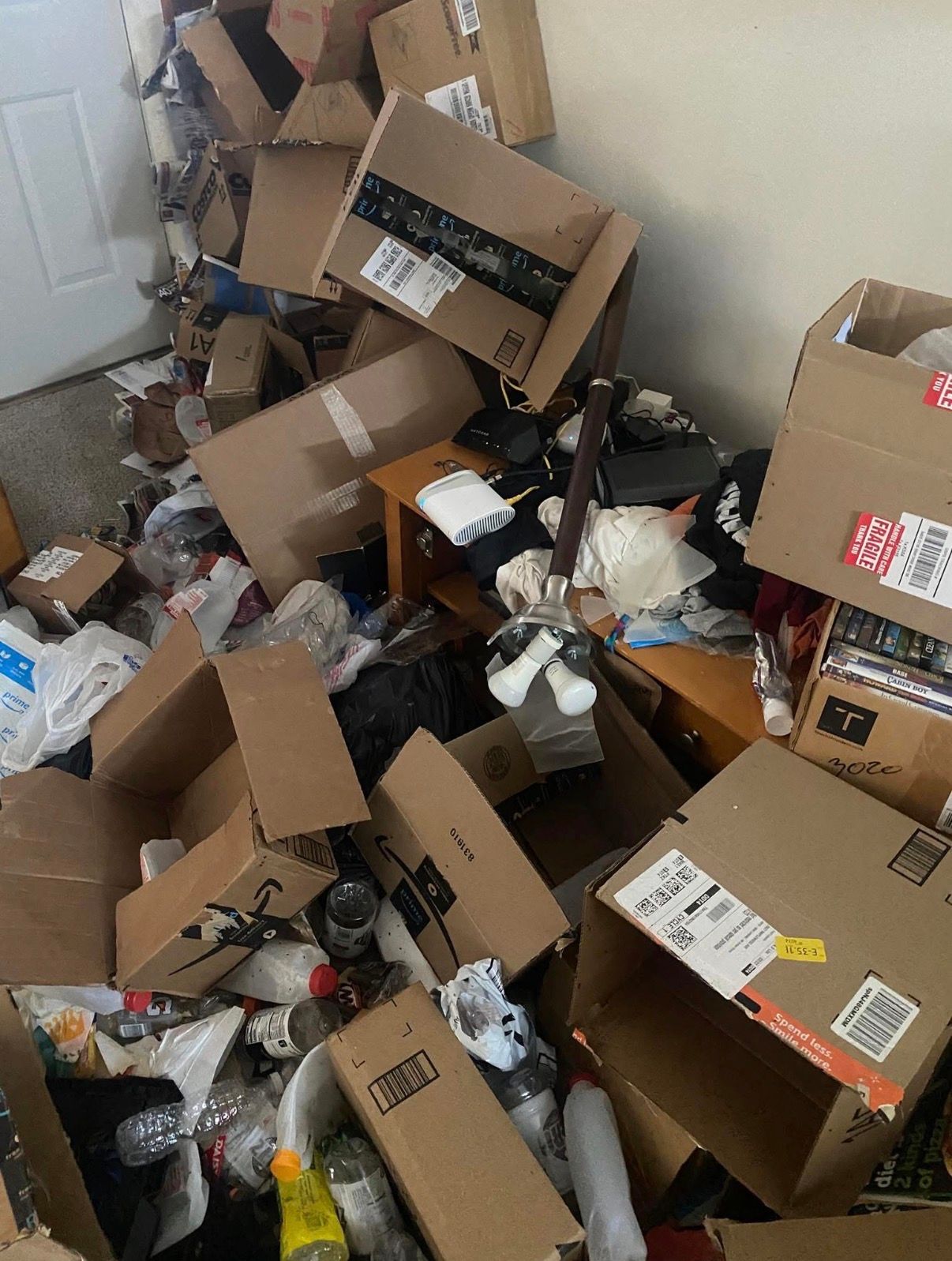 Cluttered room with piles of cardboard boxes, trash, and scattered items on the floor