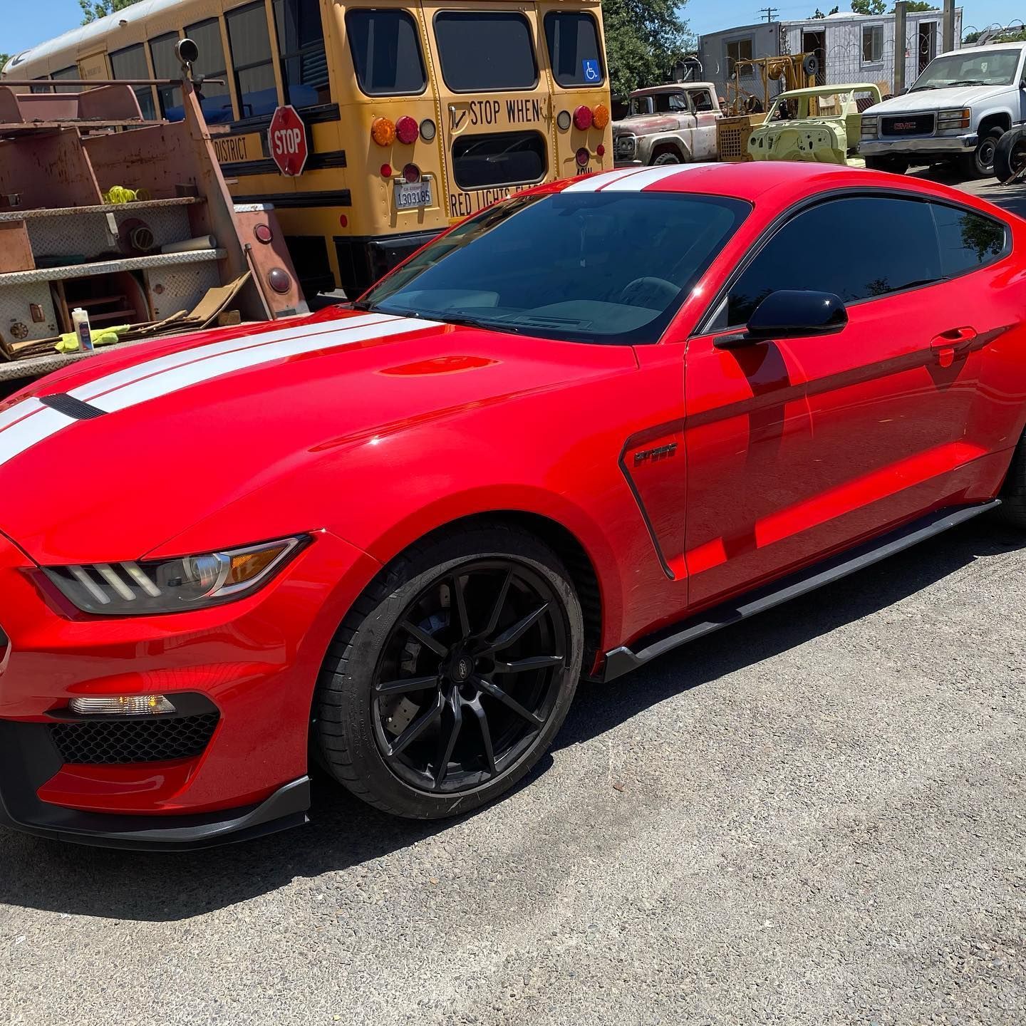 A red mustang is parked in front of a yellow school bus.