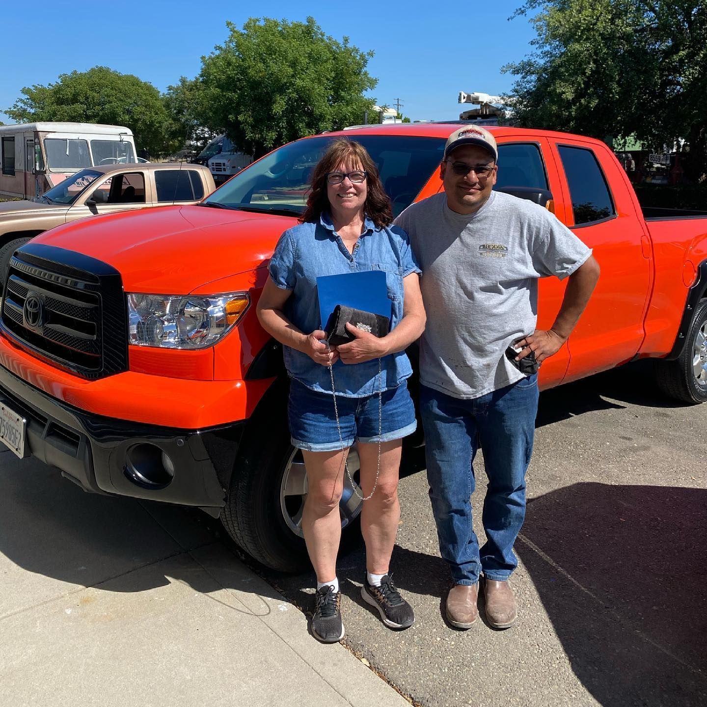 A man and a woman are standing in front of an orange truck.