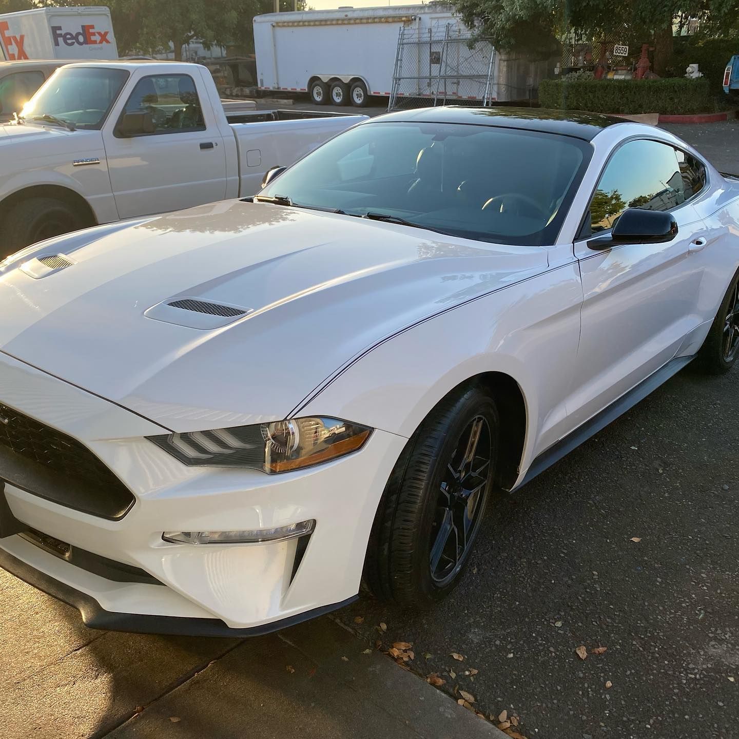 A white mustang is parked on the side of the road next to a fedex truck.