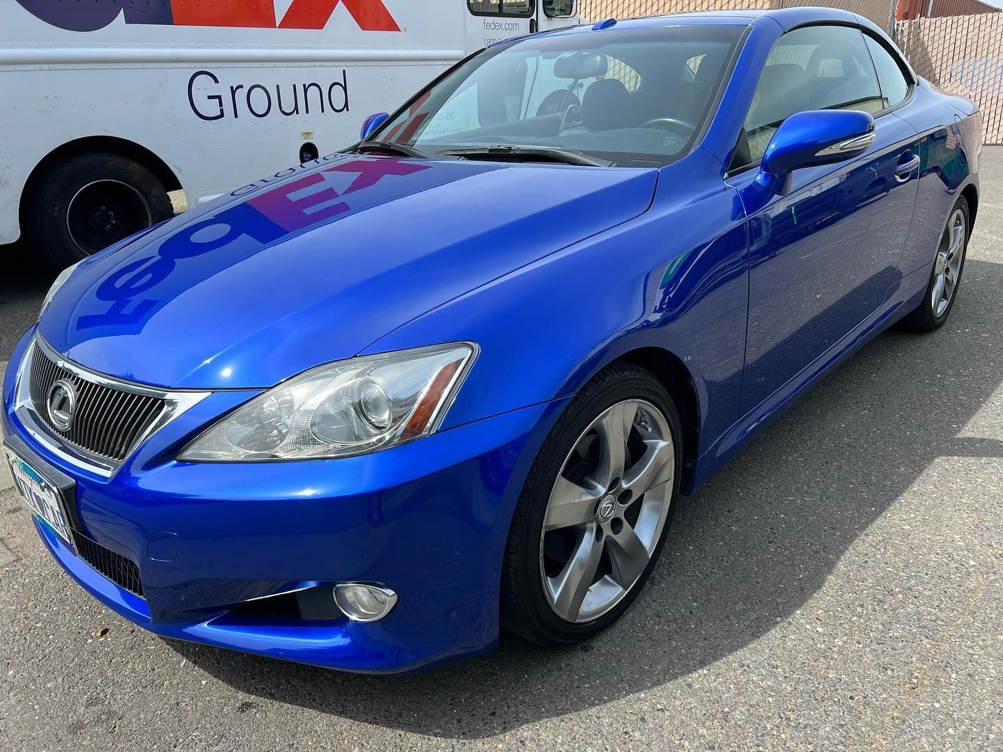 A blue car is parked in front of a fedex truck.