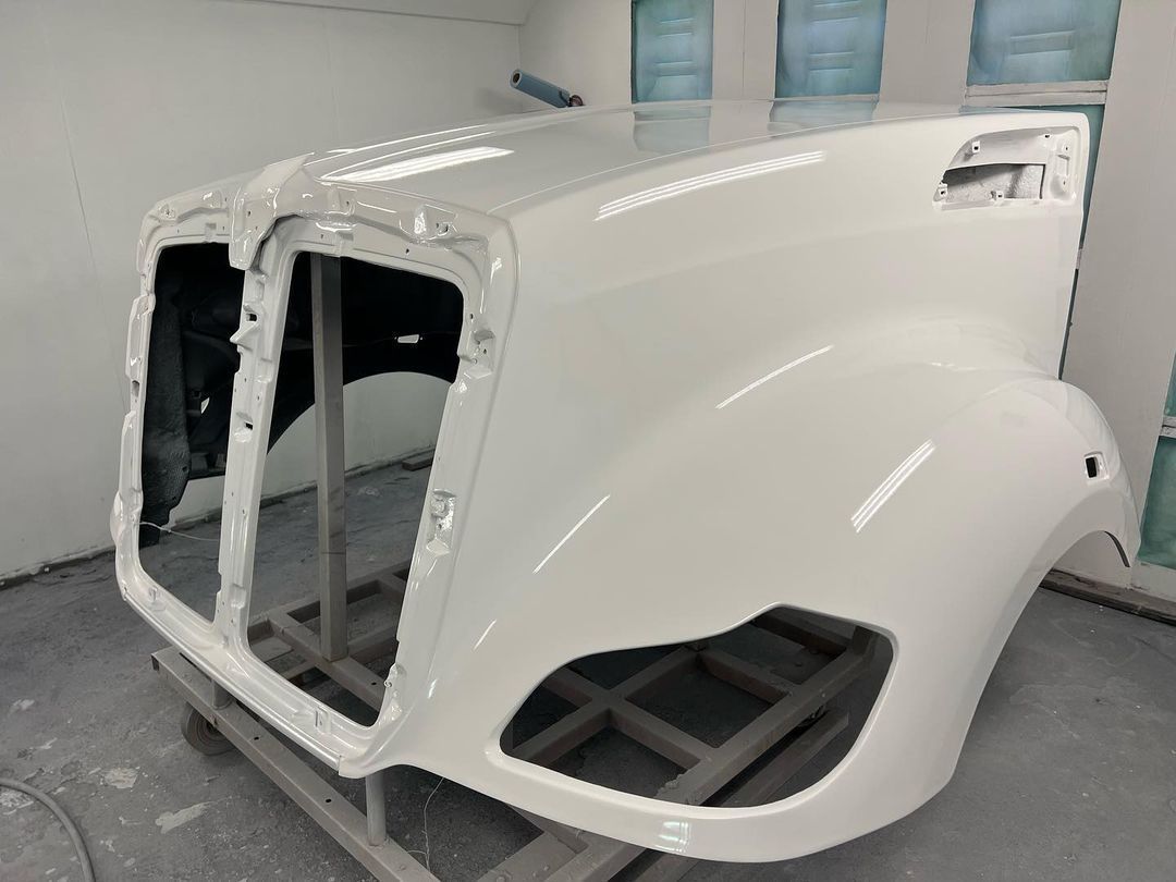 A white truck hood is sitting on a rack in a paint booth.
