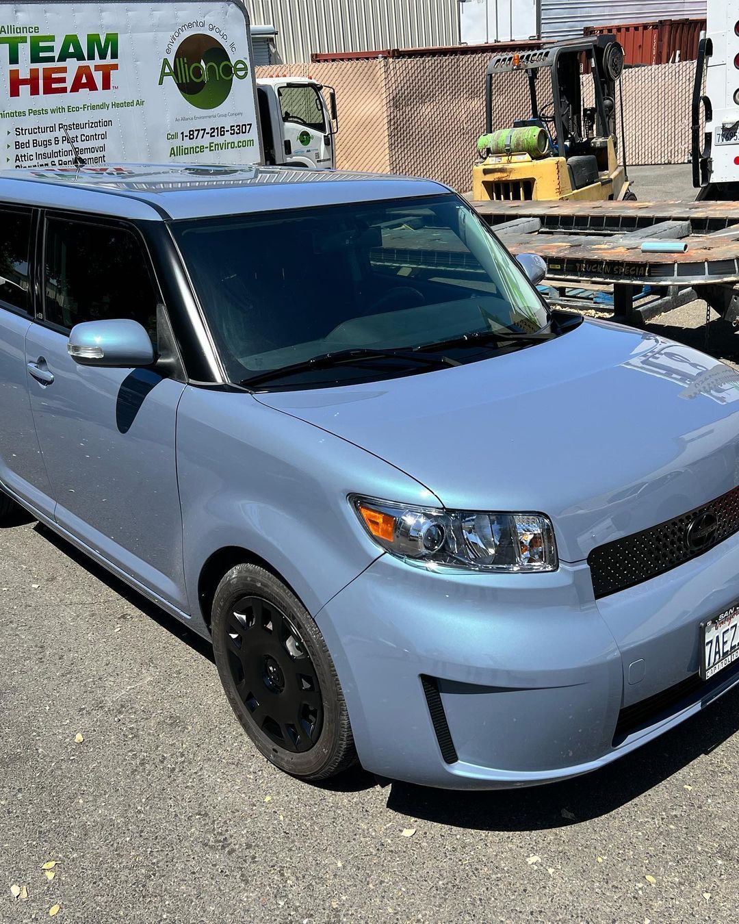 A blue car is parked in front of a truck that says team heat.