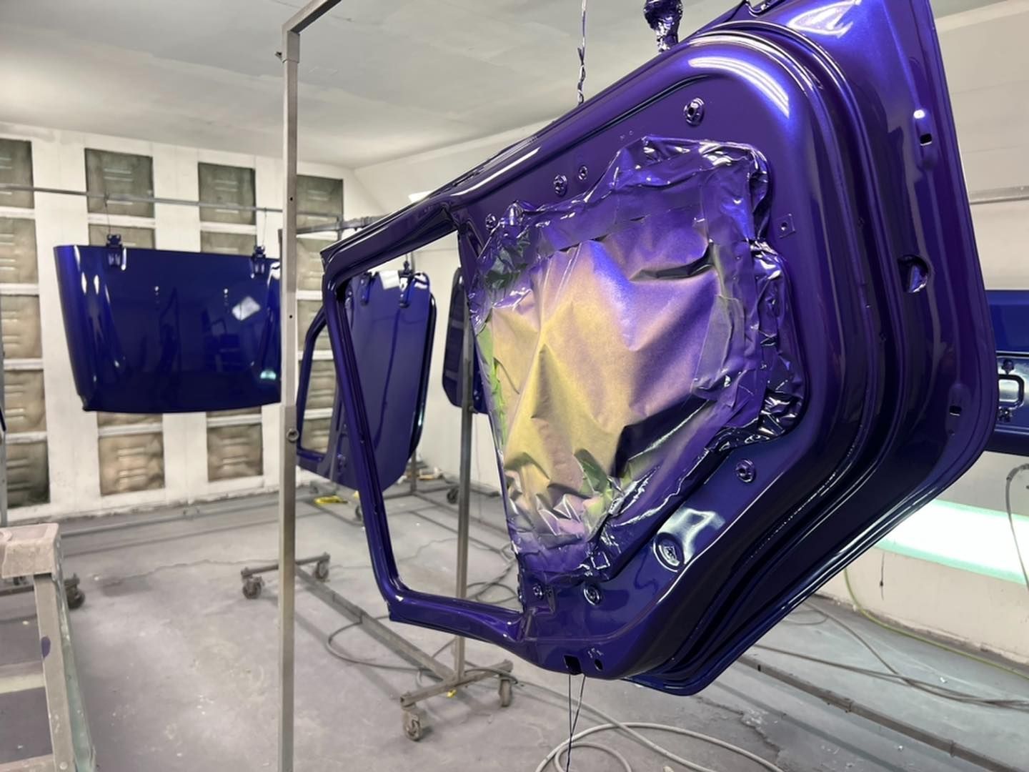 A purple car door is being painted in a paint booth.