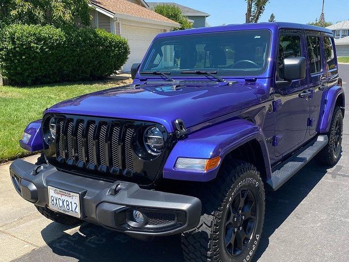 A purple jeep wrangler is parked in front of a house.