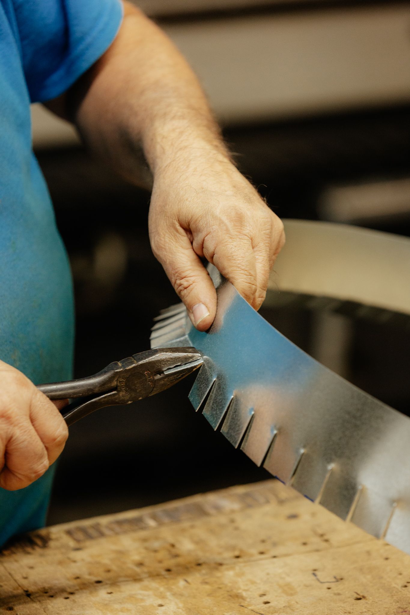 Personne utilisant des pinces pour plier une bande métallique avec des coupes régulièrement espacées.
