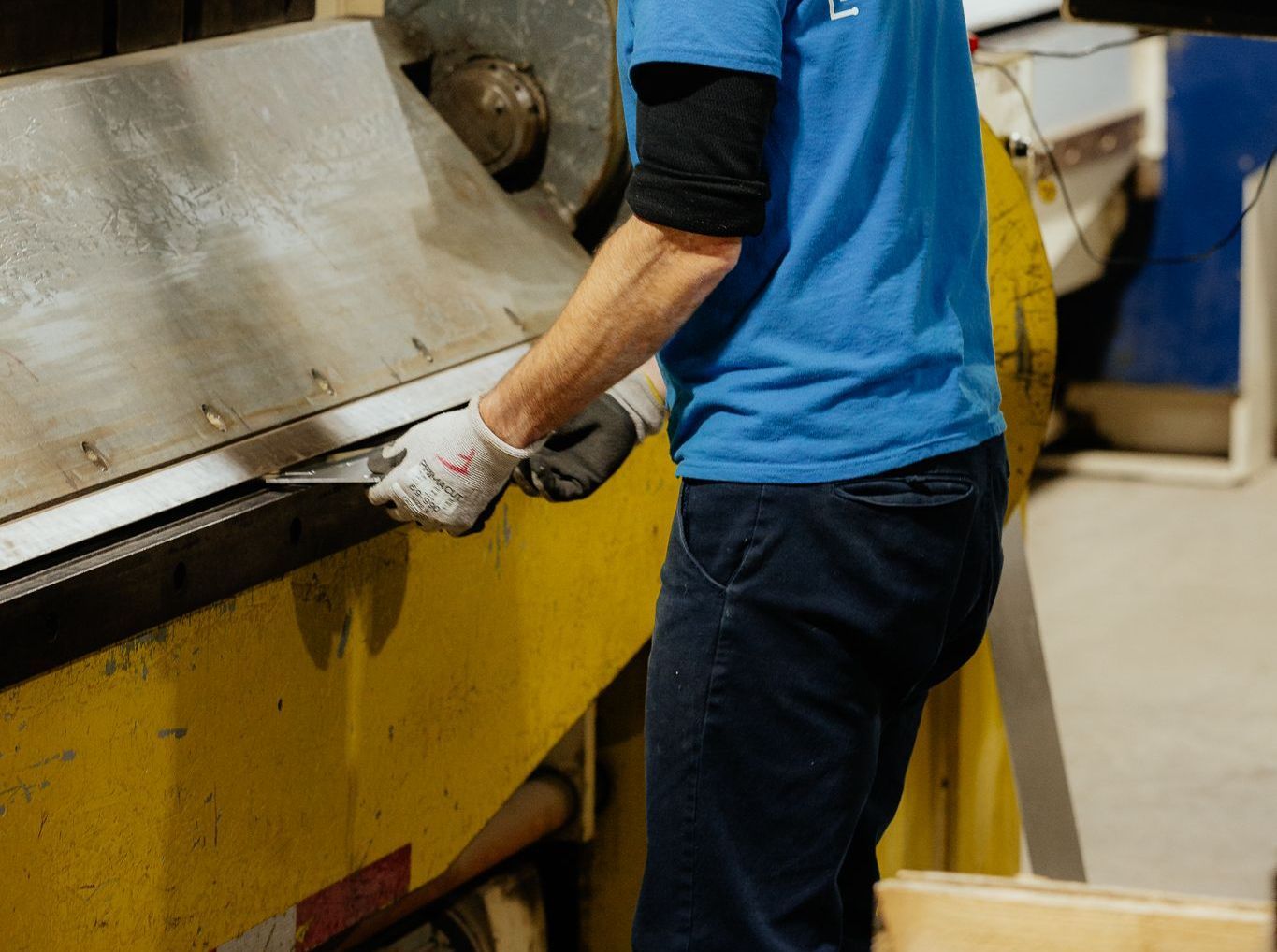 Personne portant une chemise bleue et des gants de sécurité utilisant une machine à cintrer les métaux.