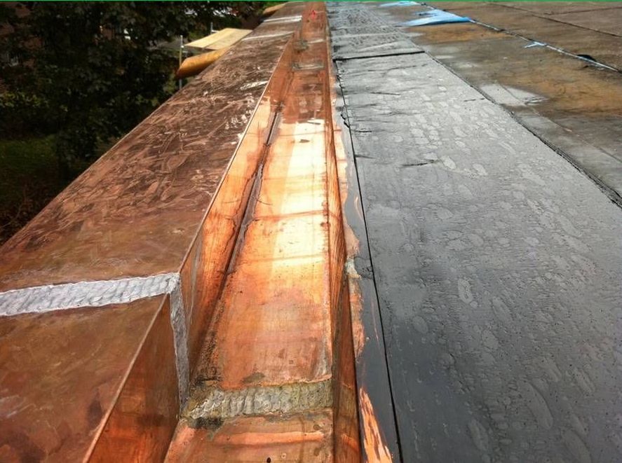 Une gouttière en cuivre est en cours d'installation sur un toit