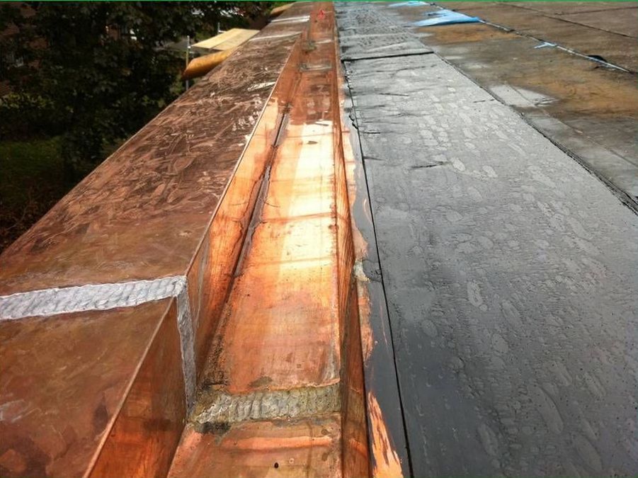 Gouttière et bordure de toit en cuivre ; métal brun clair à côté de bois sombre et patiné.