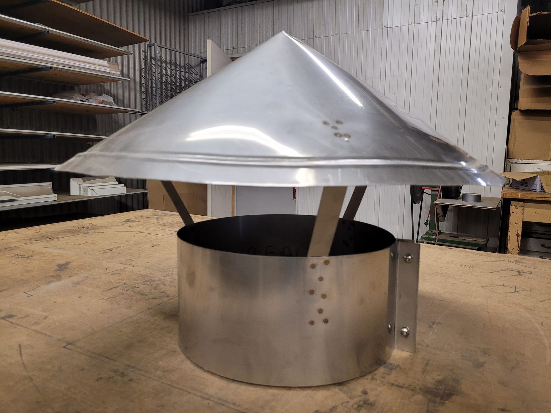 Un chapeau de cheminée en aluminium est posé sur une table en bois.