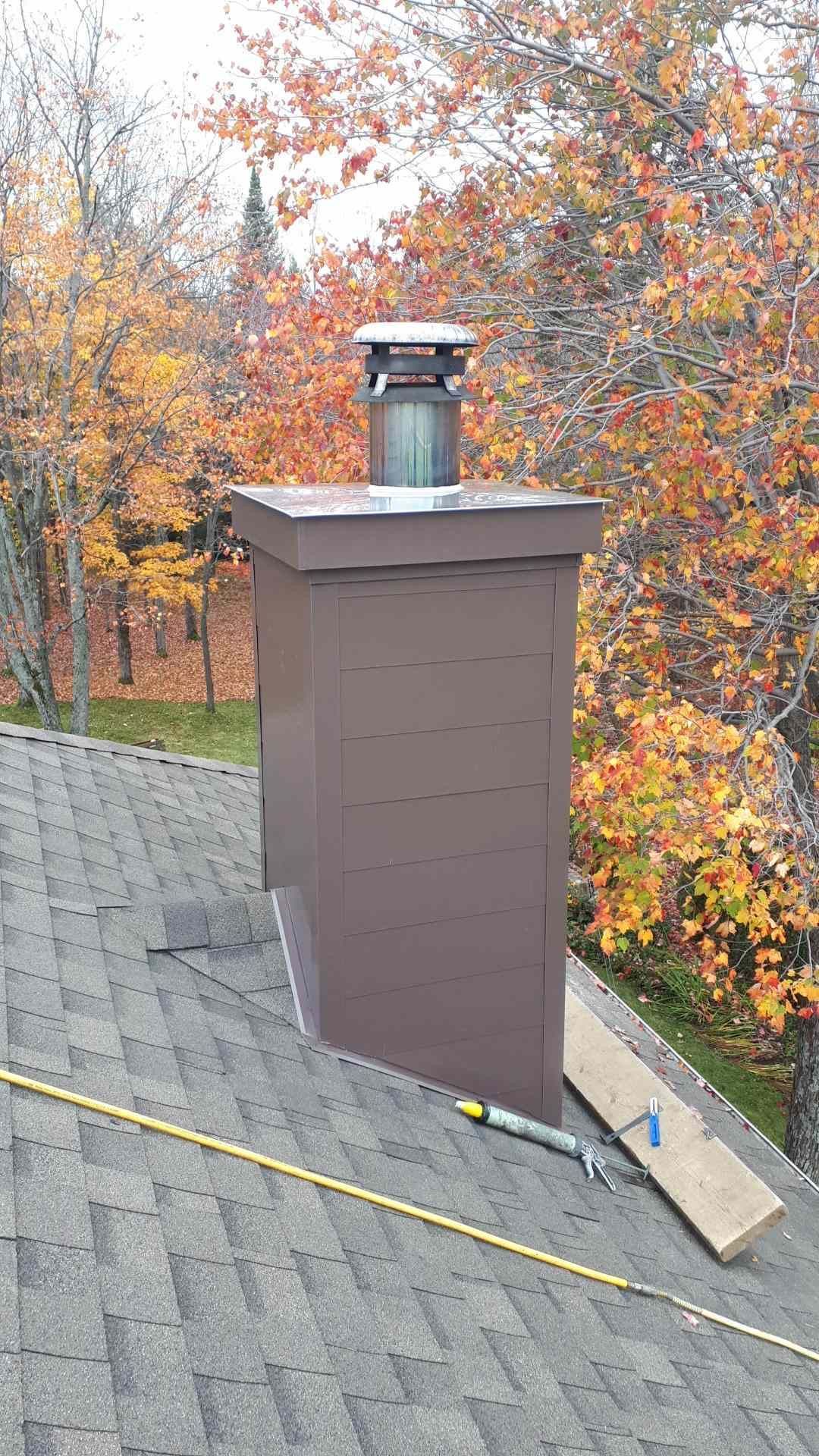 Une cheminée est posée au sommet d'un toit avec des arbres en arrière-plan.