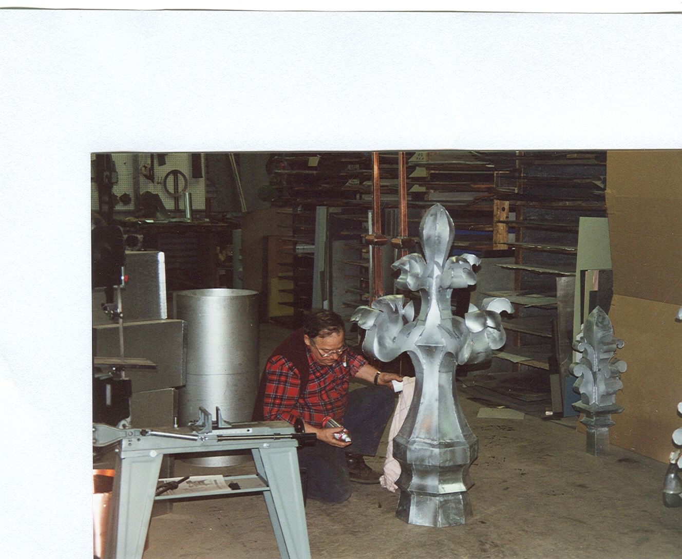 Une personne vêtue d'une chemise à carreaux rouges est agenouillée, travaillant à l'intérieur sur une grande sculpture métallique ornée.