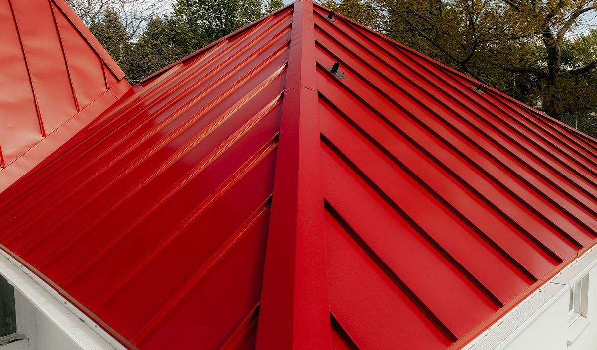 Un toit rouge sur un bâtiment blanc avec des arbres en arrière-plan.
