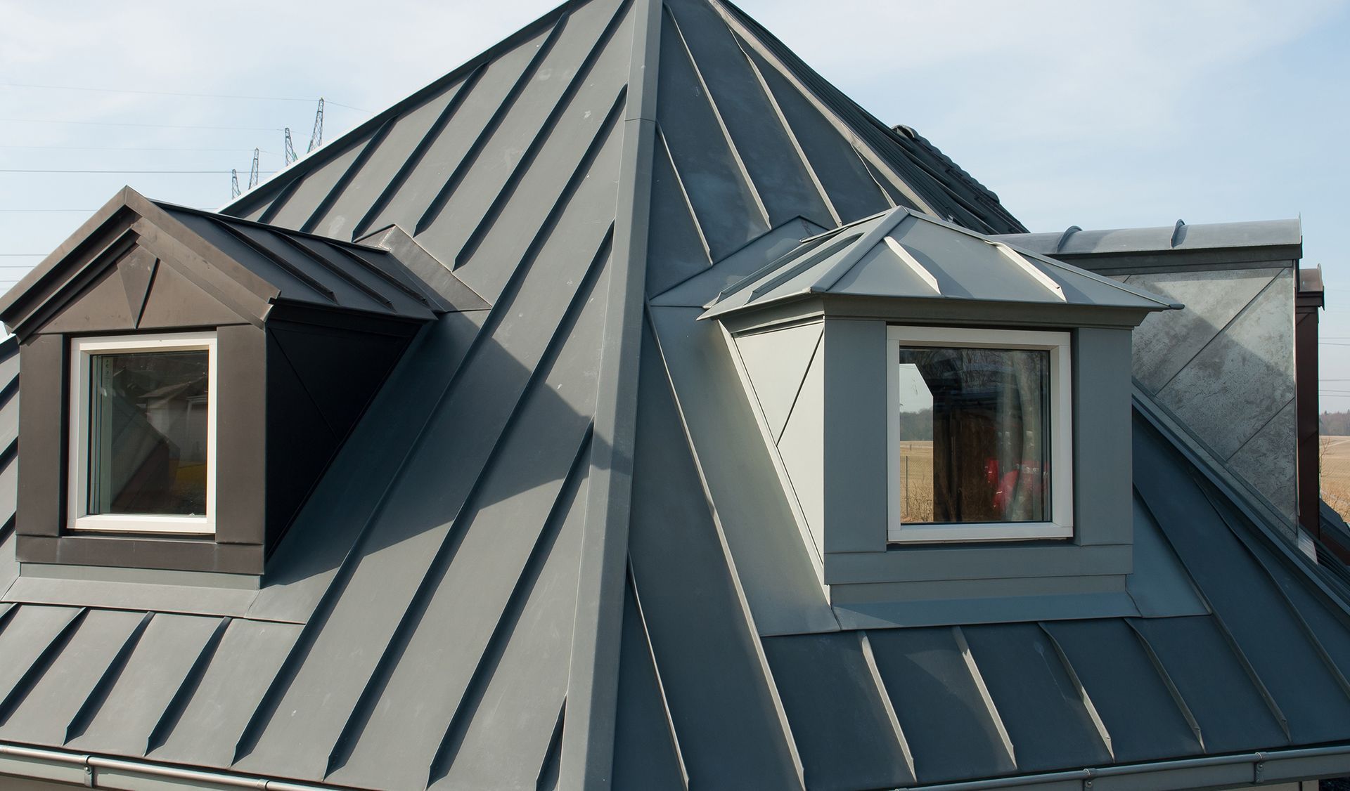 Toiture en métal gris avec deux lucarnes contre un ciel bleu.