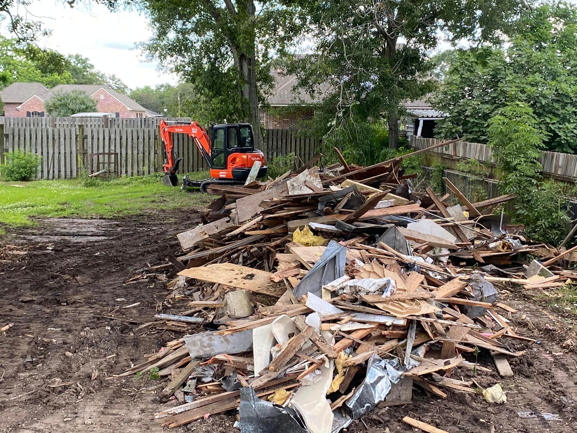 A pile of wood is sitting in the middle of a dirt field with a bulldozer in the background.
