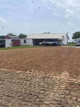 A white house is sitting on top of a dirt field next to a barn.