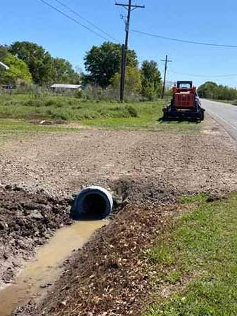 A tractor is driving down a dirt road next to a muddy pipe.