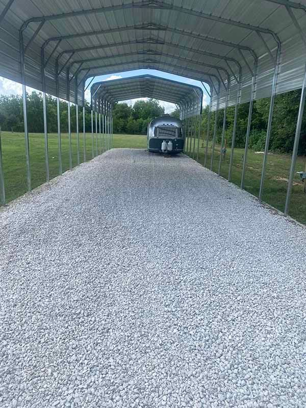 A truck is parked under a carport on a gravel road.