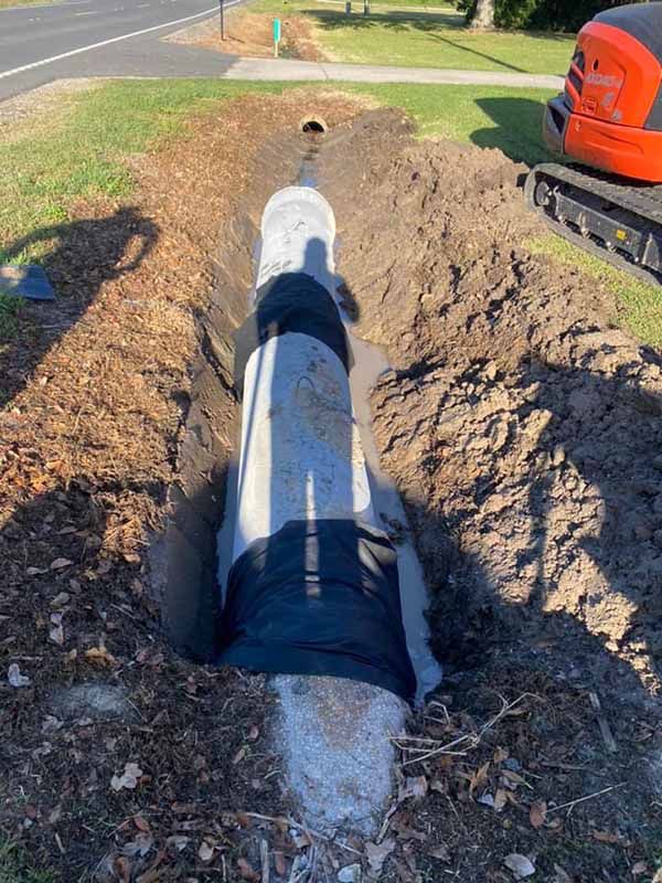 A large pipe is being installed in a trench next to a road.