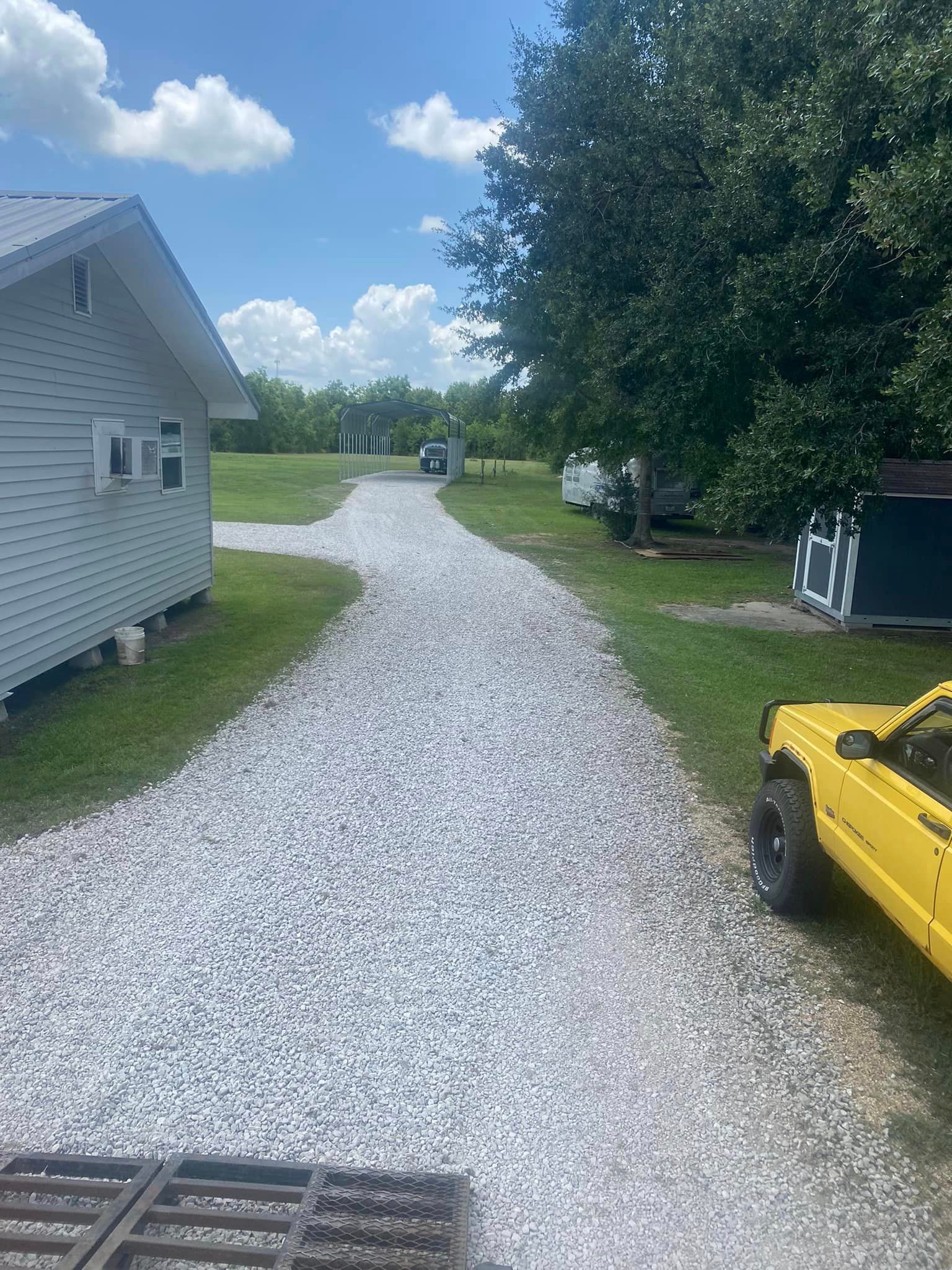 A yellow truck is parked on the side of a gravel driveway next to a house.