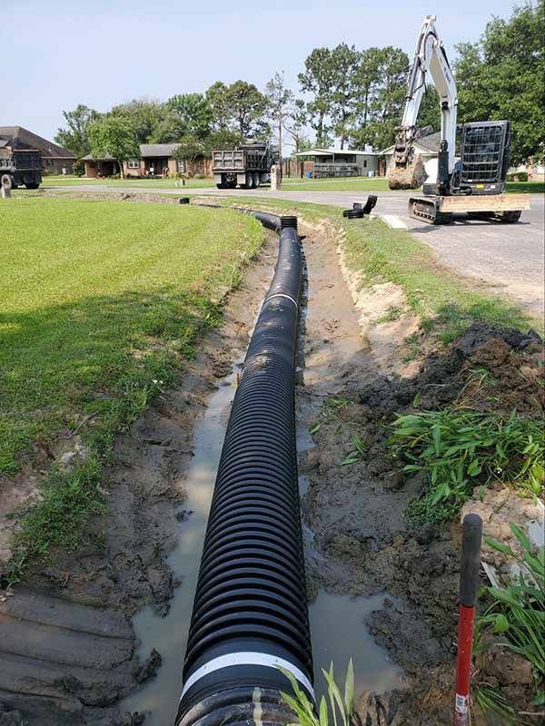 A large black pipe is being installed in a muddy field.