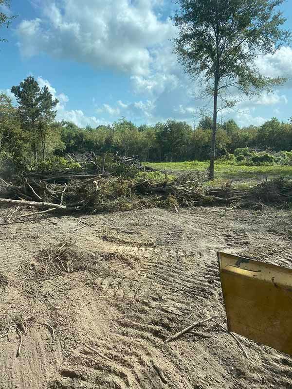 A bulldozer is driving through a dirt field with trees in the background.