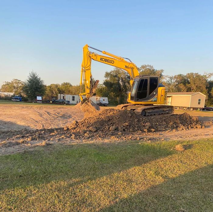 A yellow excavator is digging a hole in a field.