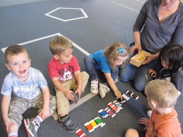 Children sitting on the floor, playing with colorful blocks, with an adult supervising
