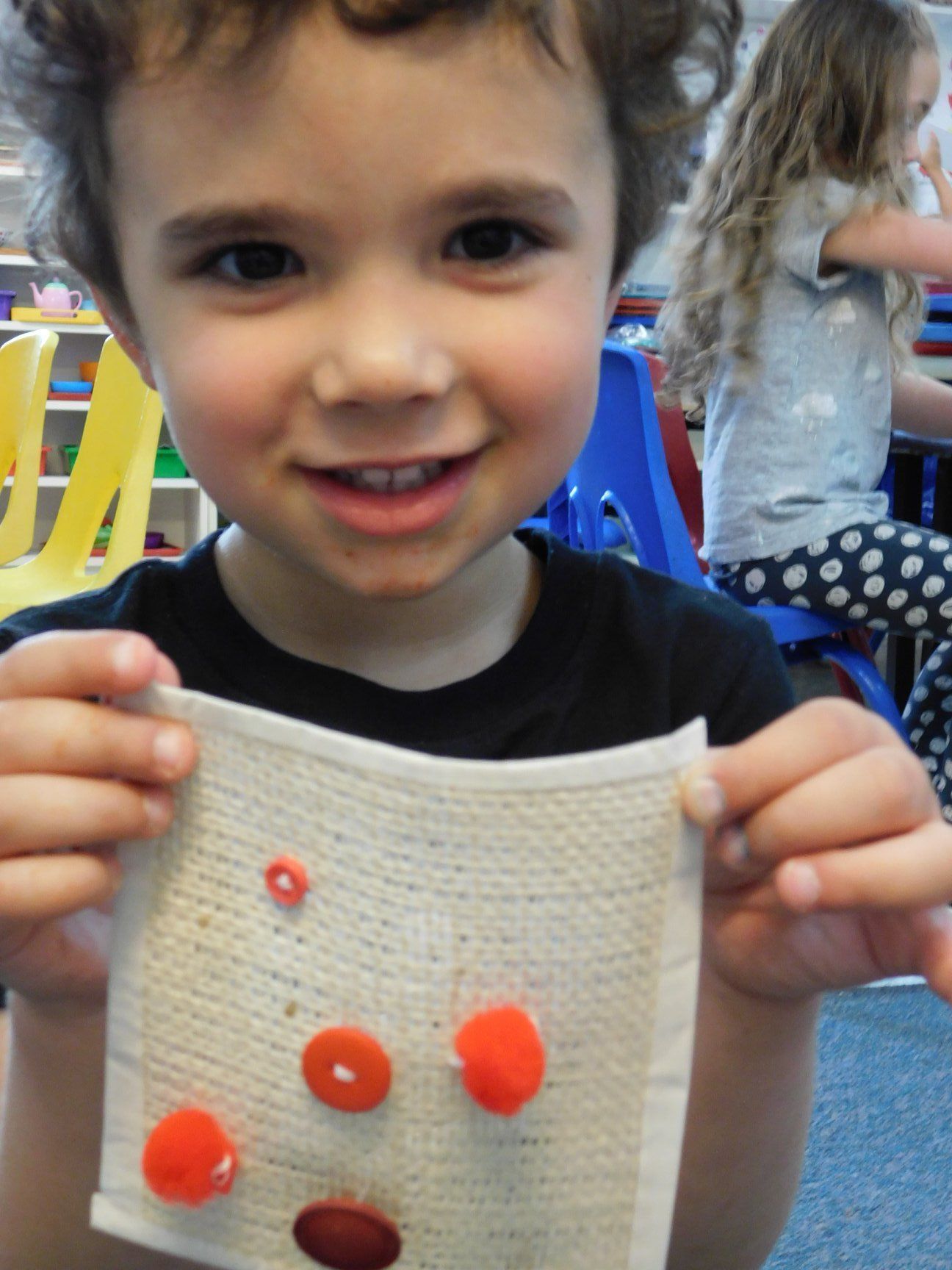 Young child smiles, holding a small fabric square with orange and red dots