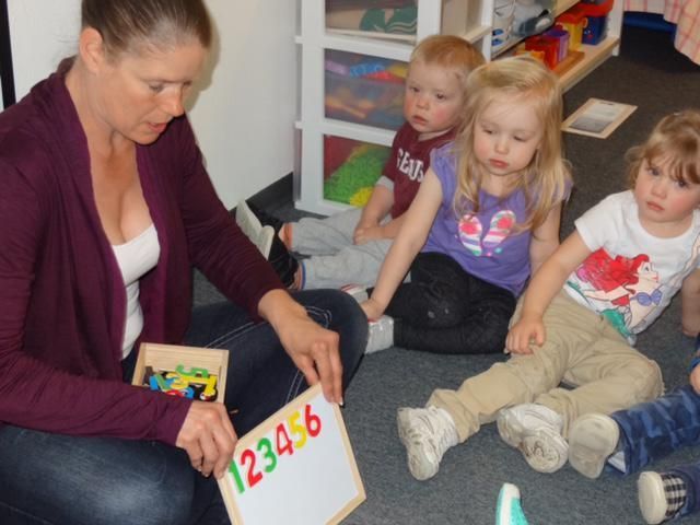 Woman teaching numbers 1-6 to children in a classroom
