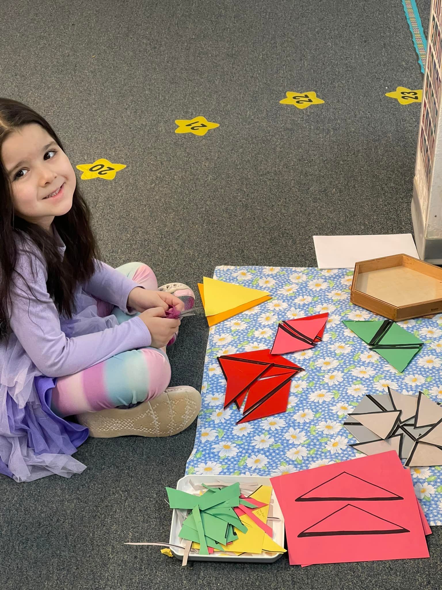 Girl smiles, surrounded by colorful geometric shapes on a patterned mat