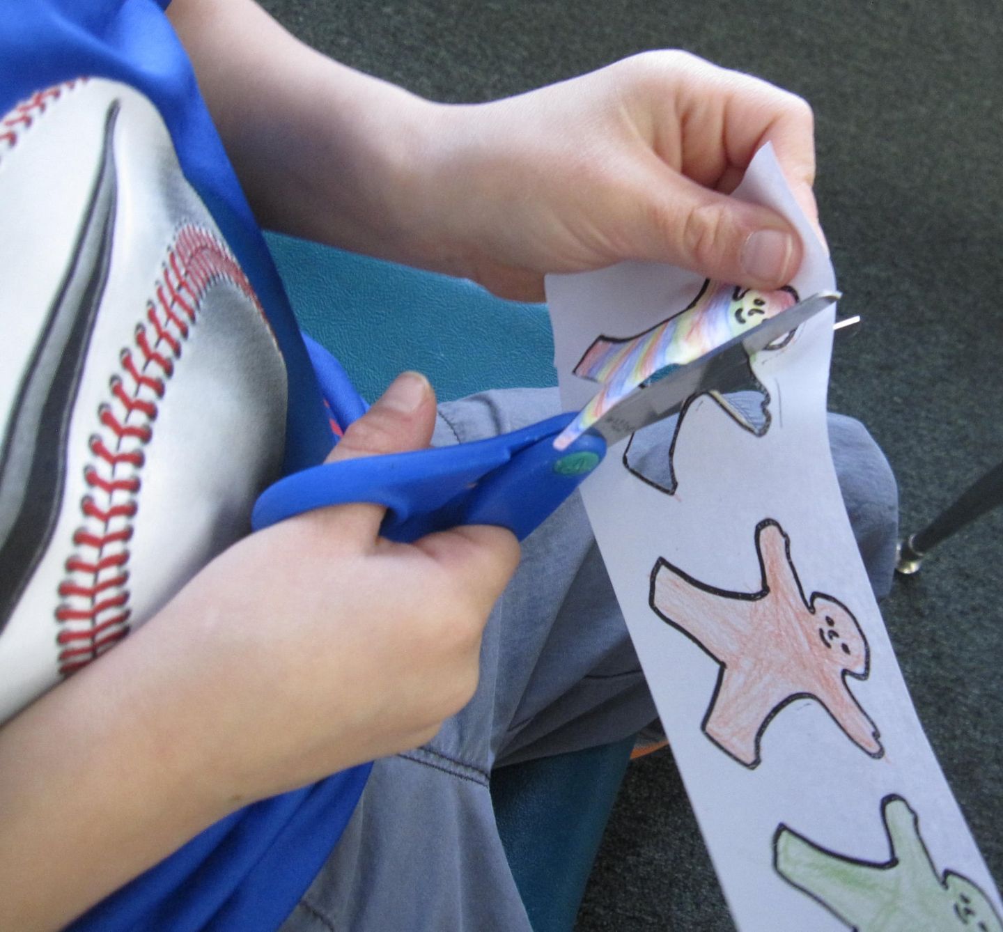Person cutting out paper figures with blue scissors