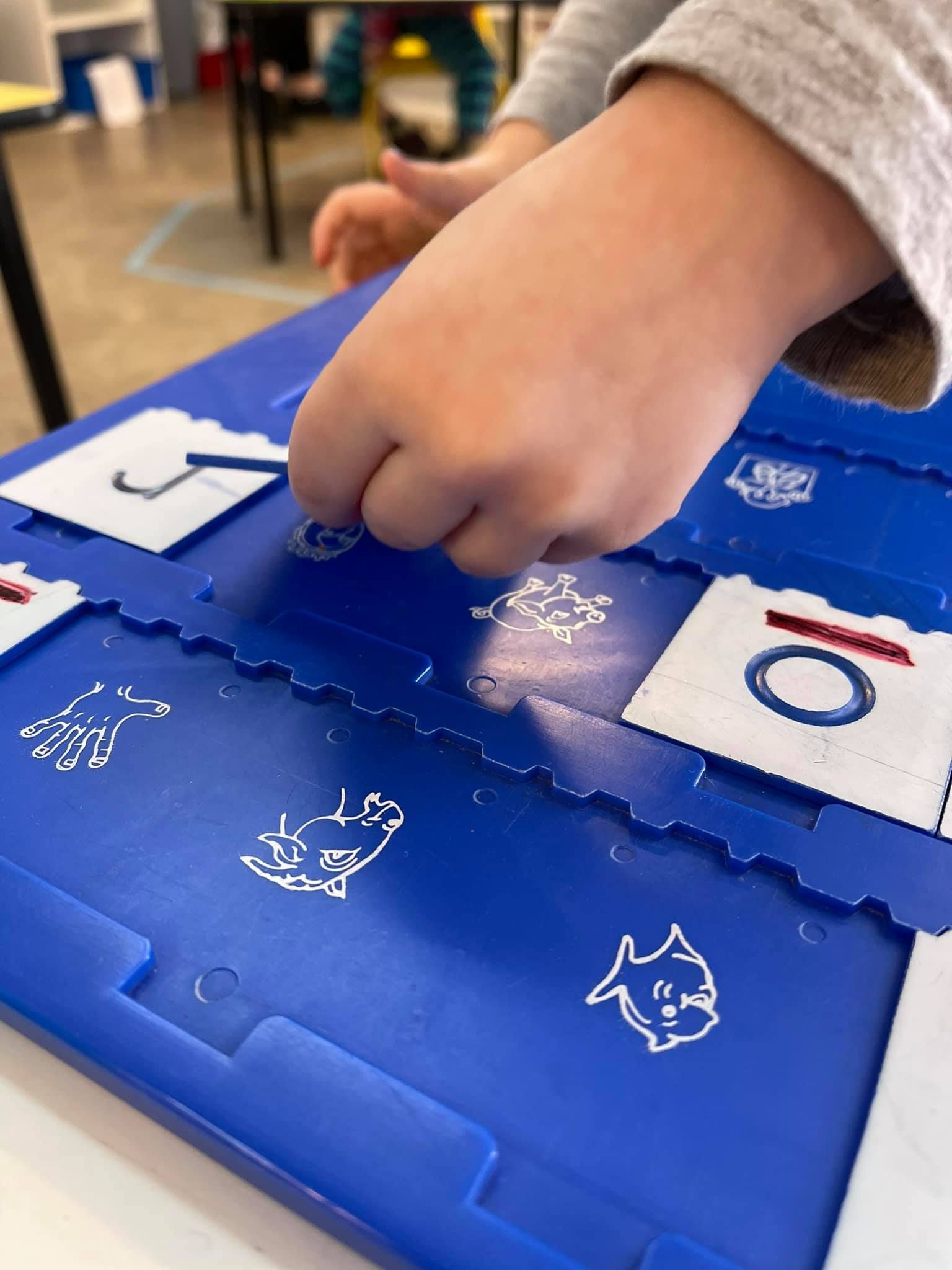 Child's hand reaching for piece on a blue toy with images of fish, a whale, a boat