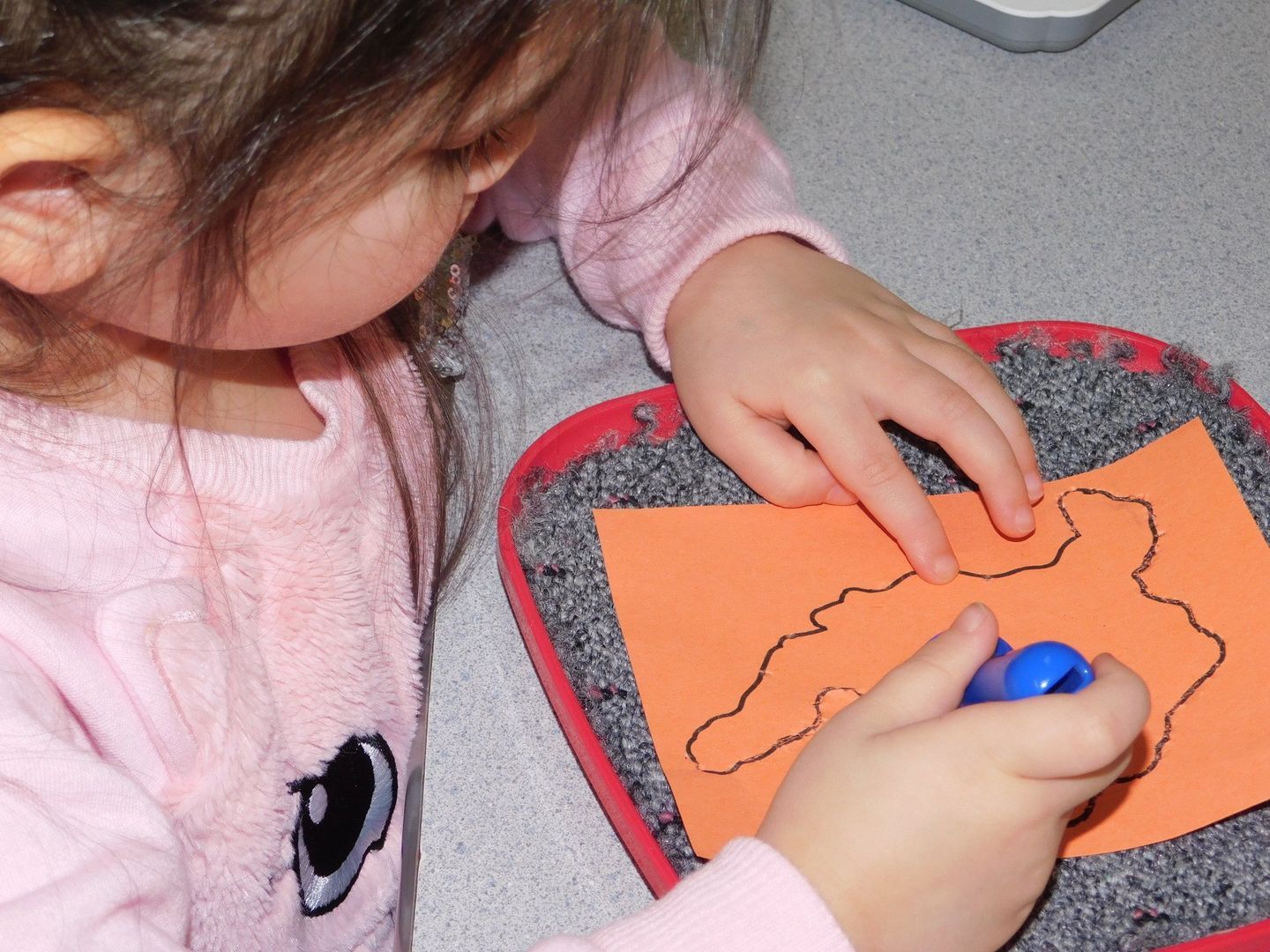 Young child using a blue marker to trace a shape on orange paper