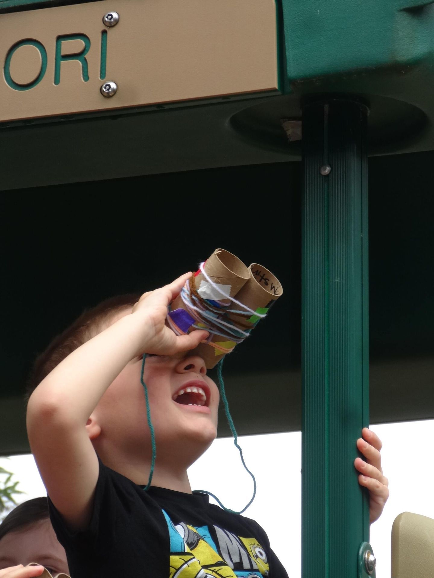 Young boy on a playground looking up through homemade binoculars made of toilet paper rolls