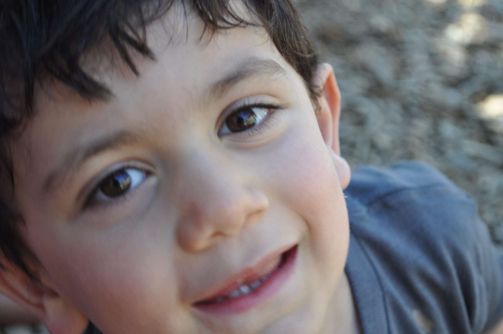 Close-up of a smiling boy with brown eyes and dark hair looking up
