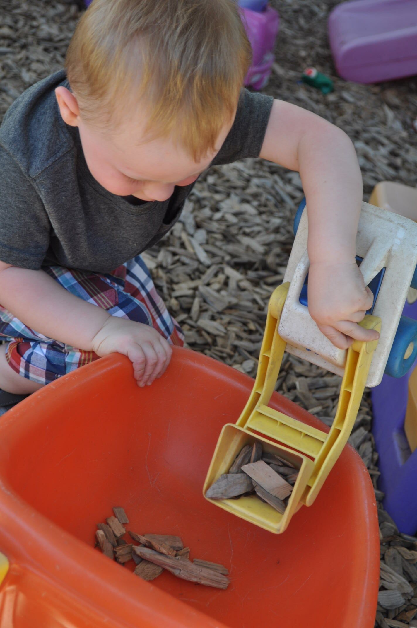 Young child with red hair playing with a yellow toy excavator