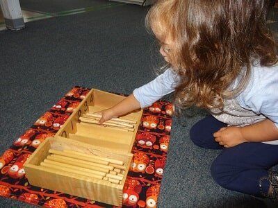 Young child playing with wooden number rods, sitting on a patterned mat