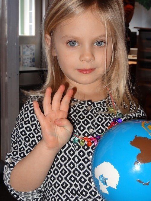Blonde girl with blue eyes holds up four fingers near a globe
