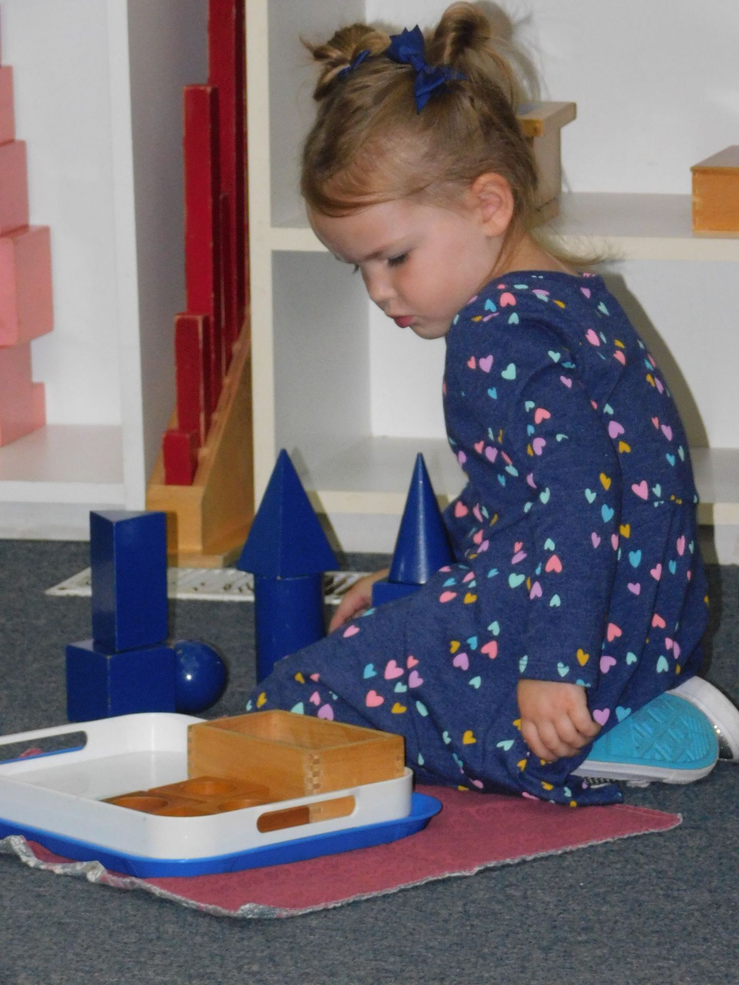Young girl in blue dress playing with blue geometric shapes, looking intently